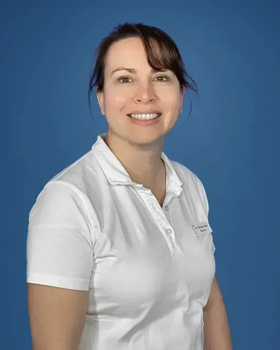 Porträt von Dr. Christine Lipke im weißen Poloshirt vor blauem Hintergrund, lächelnd.