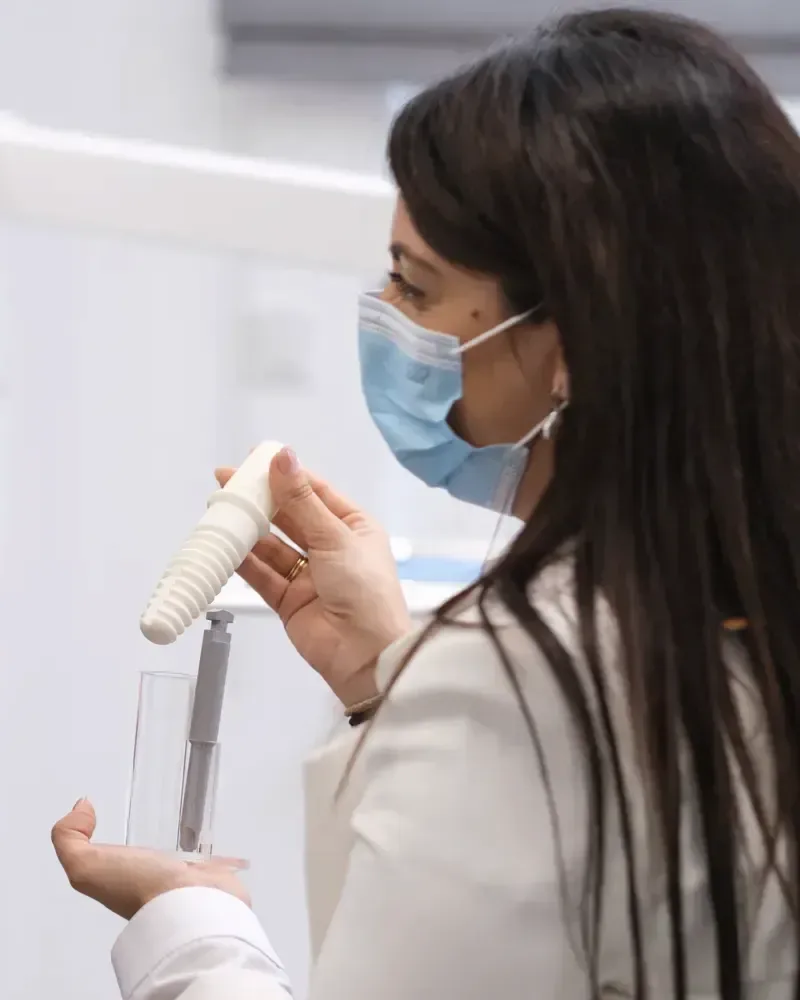 Eine Mitarbeiterin mit Mundschutz zeigt ein großes weißes Implantatmodell.