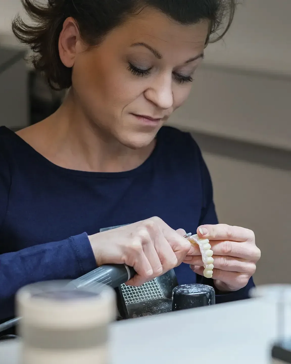 Eine Zahntechnikerin arbeitet im Labor an einer Brücke aus Keramik und hält sie zwischen den Fingern.