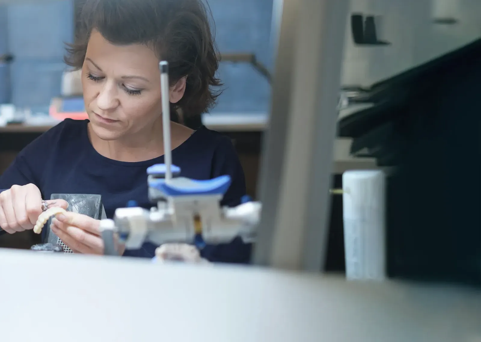 Eine Zahntechnikerin arbeitet im Labor an einer Zahnreihe, vor ihr ein Artikulator.