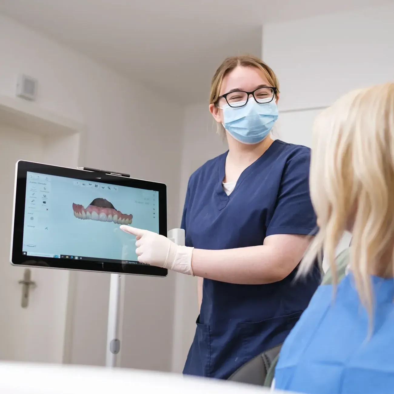 Eine Mitarbeiterin zeigt einer Patientin am Bildschirm den digitalen Scan ihrer Zahnreihe.