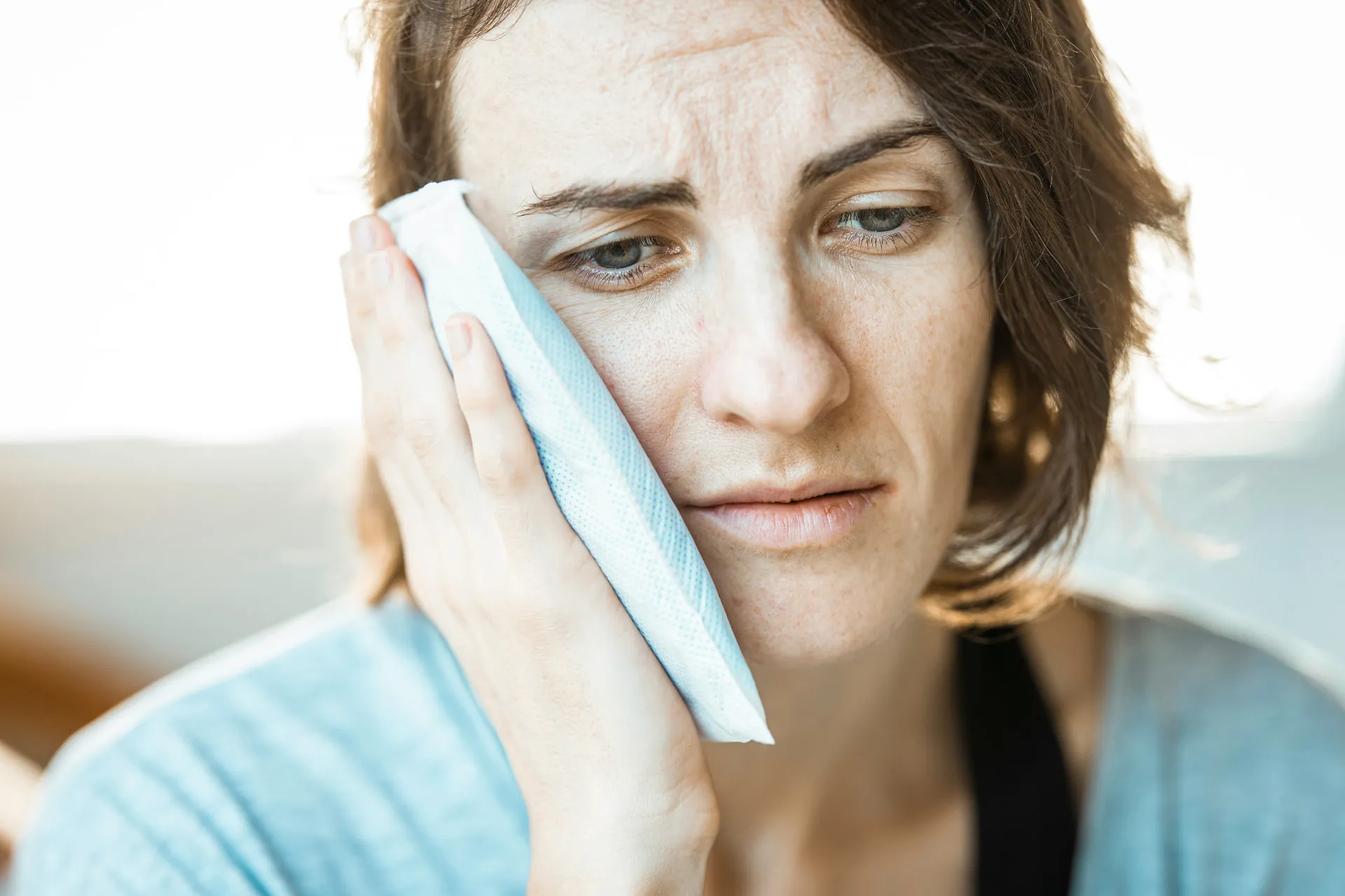 Eine Frau hält ein Kühlpad an die Wange, weil ihre Zähne schmerzen. Symbolbild.